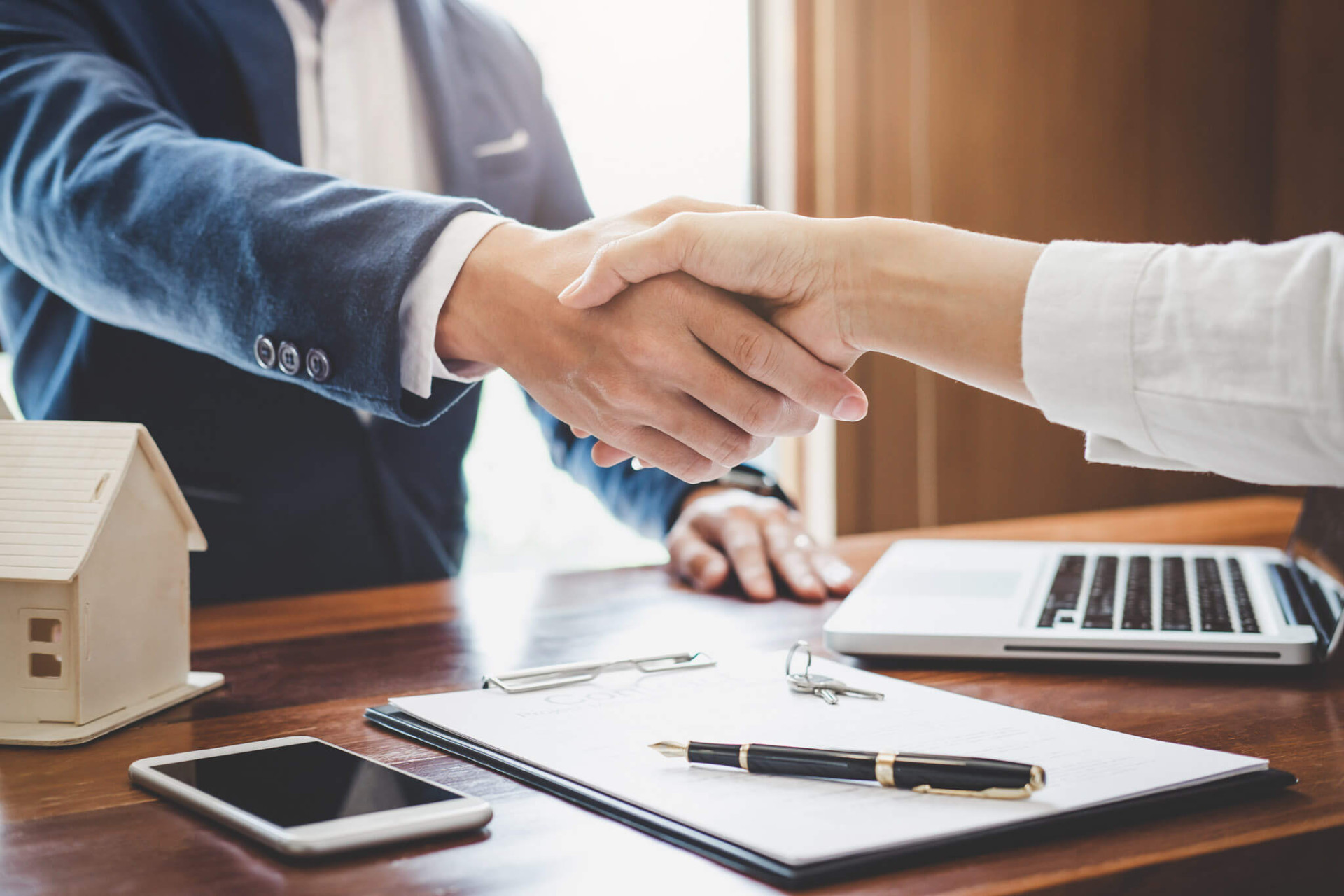 Handshake over a real estate contract beside a model house