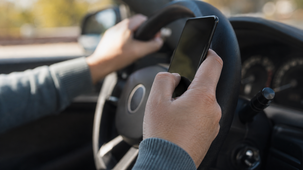 Hand holding a phone while steering a car