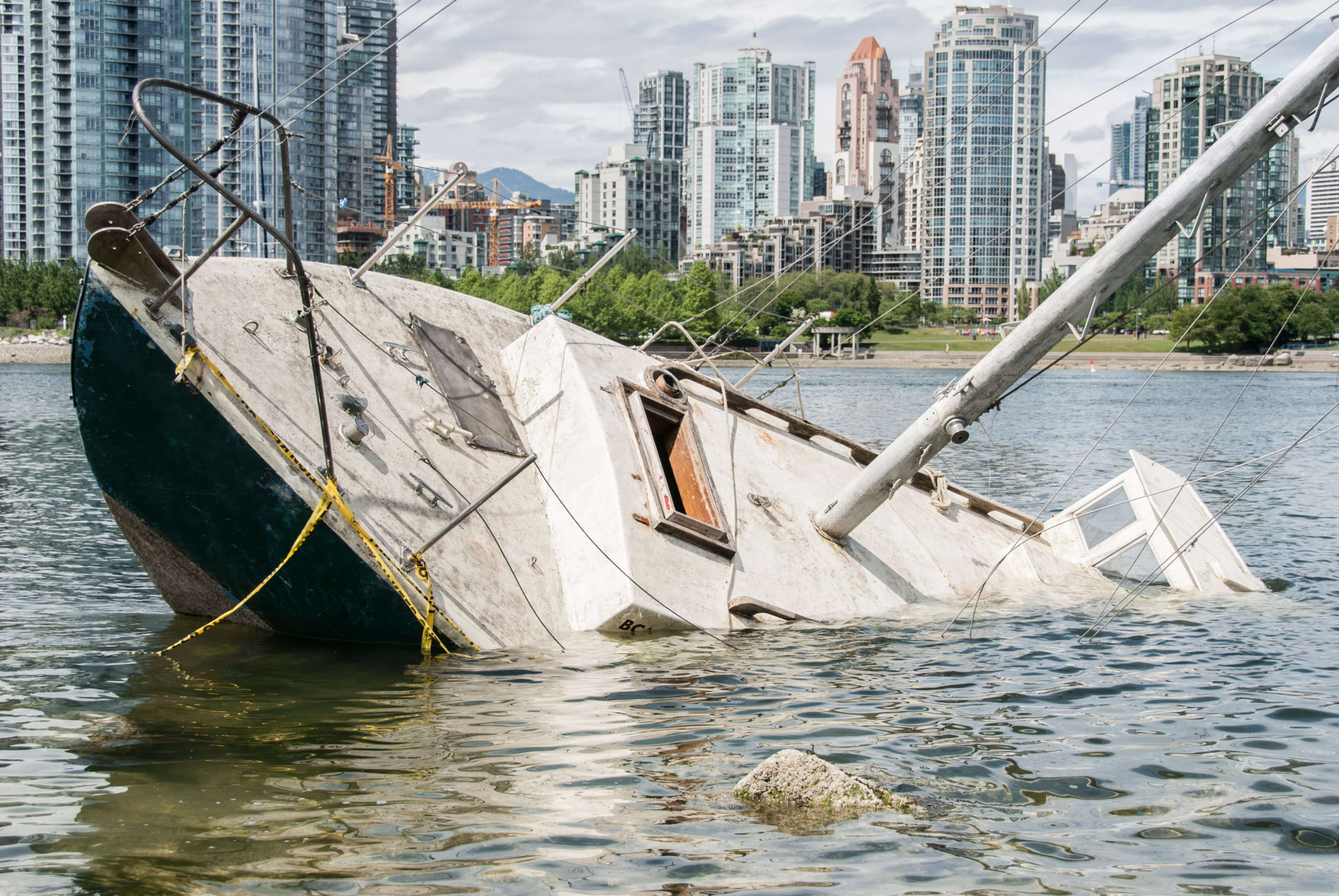 Damaged sailboat sinking near a city waterfront