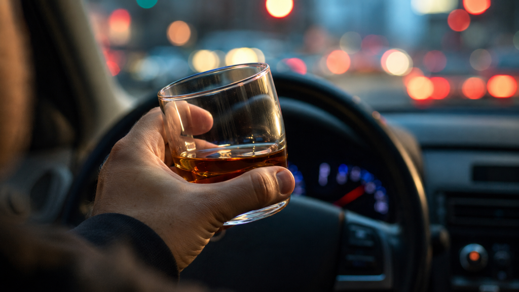 Driver holding a glass of alcohol behind the wheel